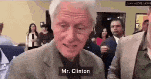 a man in a suit and tie is standing in front of a crowd and talking to mr. clinton .