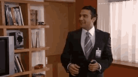 a man in a suit and tie is standing in a living room holding a cell phone .