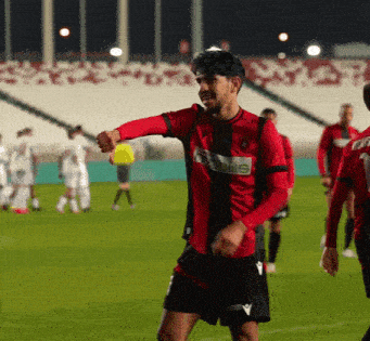 a soccer player wearing a red and black jersey with the word olis on it stands on the field