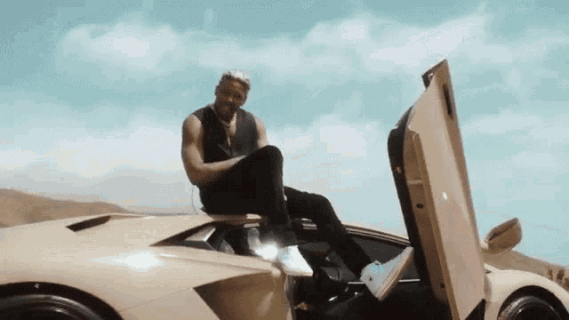 a man is sitting on the hood of a car