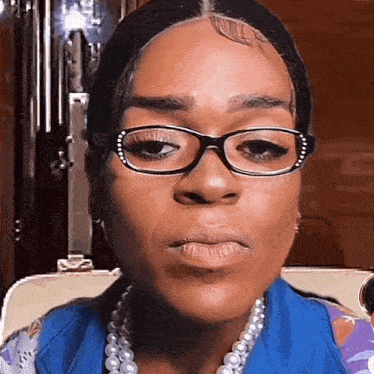 a woman wearing glasses and a pearl necklace is making a funny face