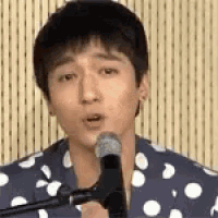 a man is singing into a microphone while wearing a polka dot shirt .