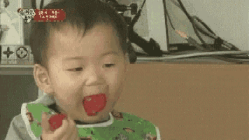 a baby in a bib is eating a red candy bar .