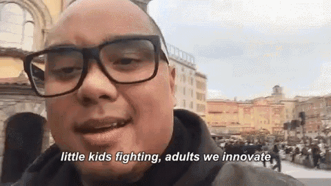 a man wearing glasses and a black jacket is talking about little kids fighting , adults we innovate .