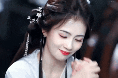 a woman in a white dress with flowers in her hair is smiling and holding her hands .