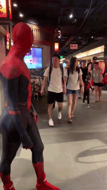 a man in a spiderman costume is walking down a hallway with people