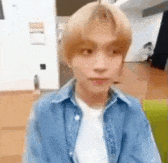 a young man wearing a blue denim jacket and a white shirt is sitting in a room .