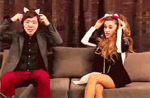 a man and a woman are sitting on a couch and the man is wearing a cat ear headband .