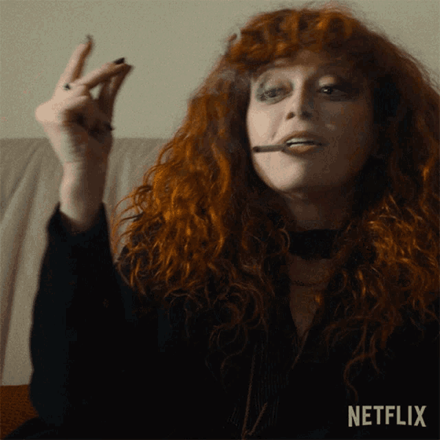 a woman with red hair is smoking a cigarette with netflix written on the bottom