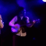 a man is playing a banjo in a dark room with purple lights behind him