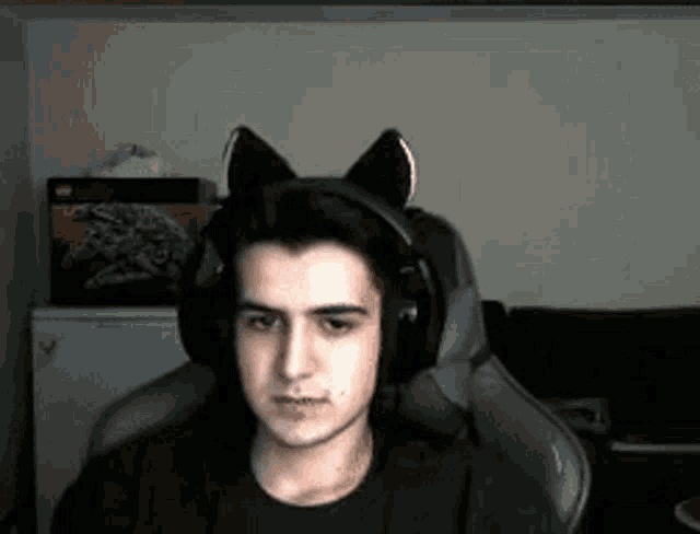 a young man wearing headphones with cat ears on his head is sitting in a chair .