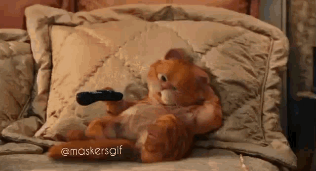 garfield the cat is laying on a bed with a remote control in his hand .