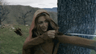 a woman in a red hood is holding a bow and arrow in front of a tree