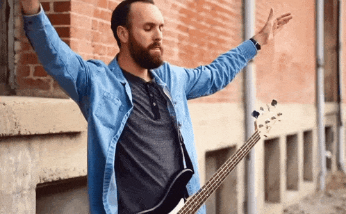 a man in a blue shirt is holding a bass guitar in front of a brick wall