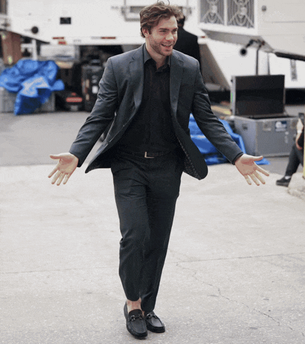 a man in a suit stands with his arms outstretched in front of a blue tarp
