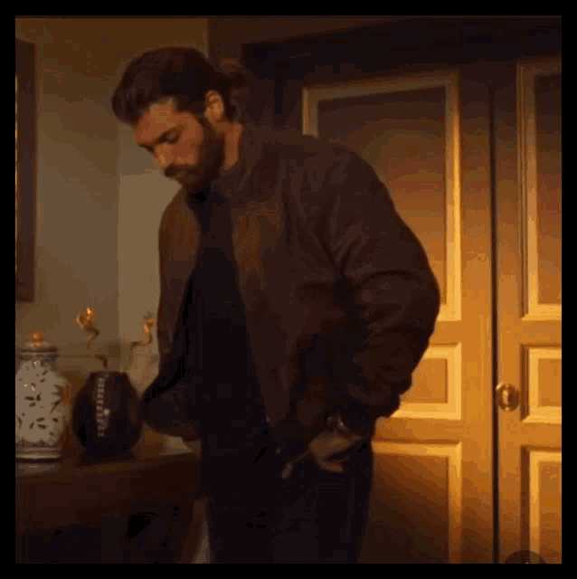 a man in a brown jacket is standing in front of a door with his hands in his pockets