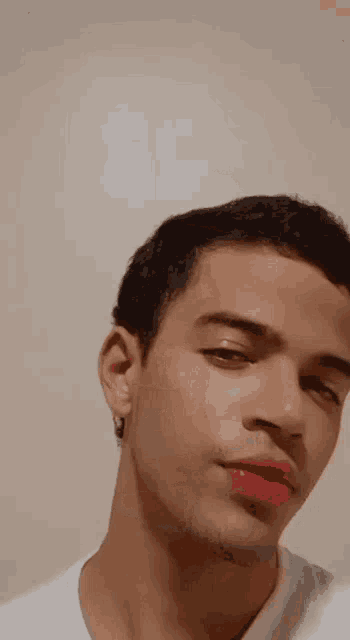 a young man wearing red lipstick and earrings is making a funny face .