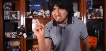 a man in a blue shirt is making a funny face while standing in front of a shelf full of video games .