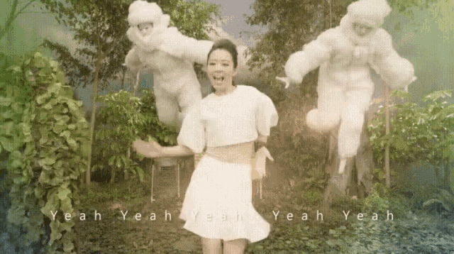 a woman in a white dress is jumping in the air in front of a group of white ghosts .