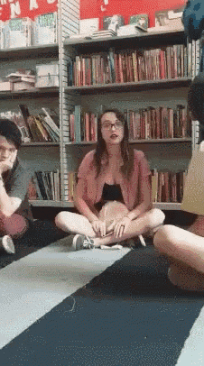 a group of people are sitting on the floor in front of a bookshelf