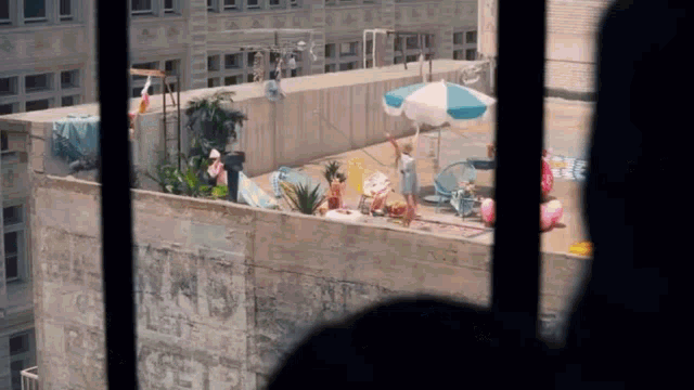 a view of a rooftop party from a window with umbrellas and chairs .