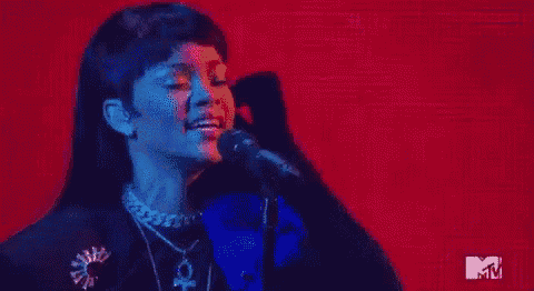a woman is singing into a microphone on a stage in front of a red background .