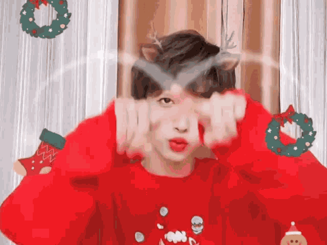 a young man wearing a red sweater with reindeer antlers is making a funny face .