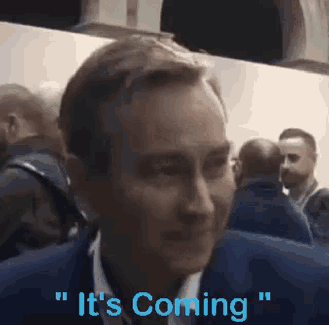 a man in a suit says it 's coming while standing in a crowd .