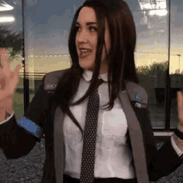 a woman in a suit and tie is standing in front of a building and waving .