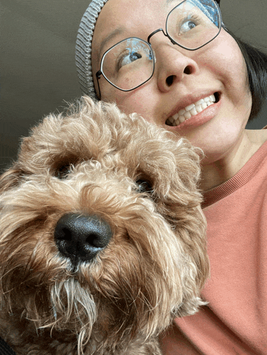 a woman wearing glasses and a beanie is holding a small brown dog