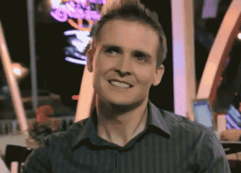 a man in a striped shirt is smiling in front of a neon sign that says ' g ' on it