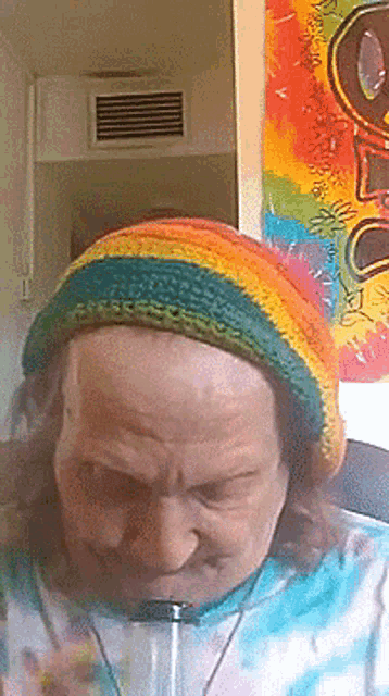 a man wearing a rainbow hat and tie dye shirt is smoking a pipe