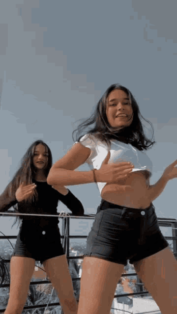 two young women are dancing on a balcony and one is wearing shorts