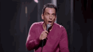 a man in a purple sweater is holding a microphone and speaking into it .