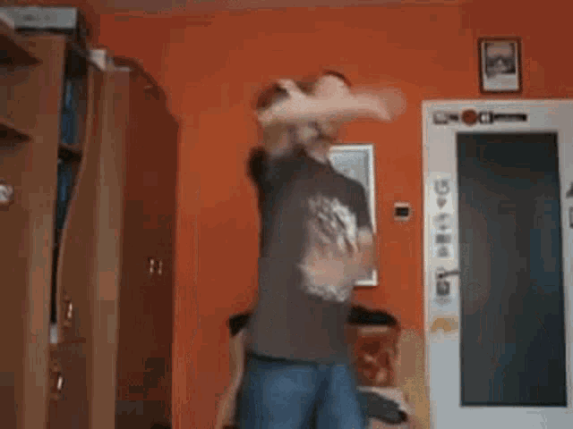 a man in a brown shirt is dancing in a living room while another man in underwear is standing in the background .
