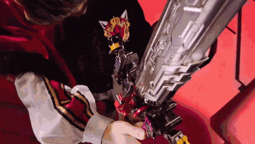 a person in a red cape is holding a large sword with a crown on it .