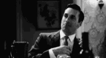 a man in a suit and tie is sitting at a table with a bottle of wine and a glass .