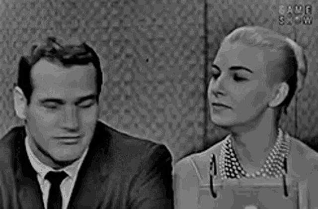 a man and a woman are sitting next to each other and looking at each other in a black and white photo .