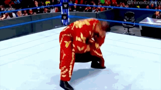 a wrestler in a red suit is kneeling down in a wrestling ring .