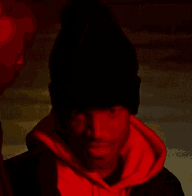 a man wearing a black hat and a red hoodie is smiling in a dark room .