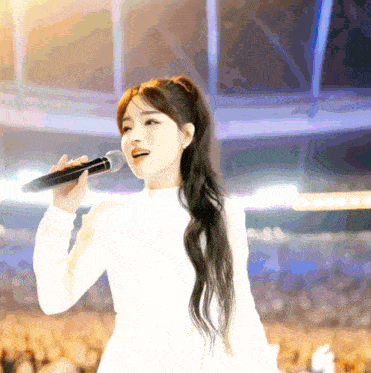 a woman singing into a microphone while wearing a white dress