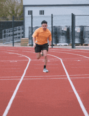 a man in an orange shirt and black shorts runs on a track