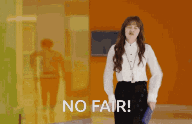 a woman in a white shirt and black pants is standing in front of an orange wall with the words no fair written on it