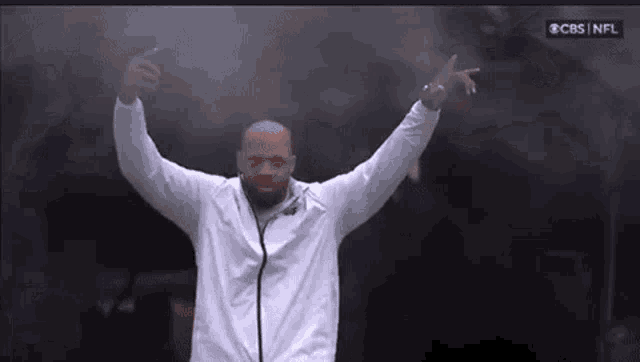 a man in a white jacket is standing in front of a microphone with his arms outstretched .