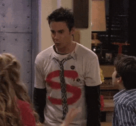 a man wearing a tie and a t-shirt with the letter s on it is standing in a room with two children .