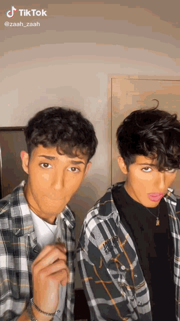two young men are making funny faces with their tongues out while wearing plaid shirts .