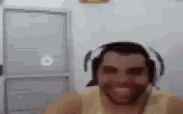 a man with a beard wearing headphones and a yellow tank top is smiling .