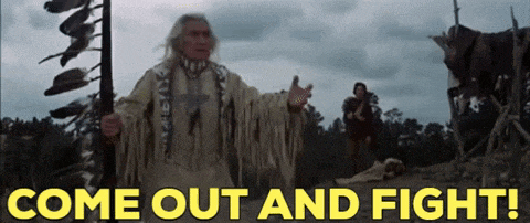 a man in a native american outfit is holding a gun in front of a sign that says come out and fight
