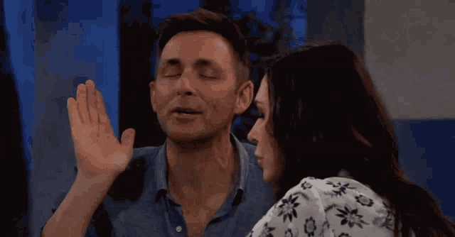 a man and a woman are looking at each other and the woman is whispering into the man 's ear
