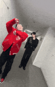 a man in a red jacket is standing next to another man in a black suit in a hallway